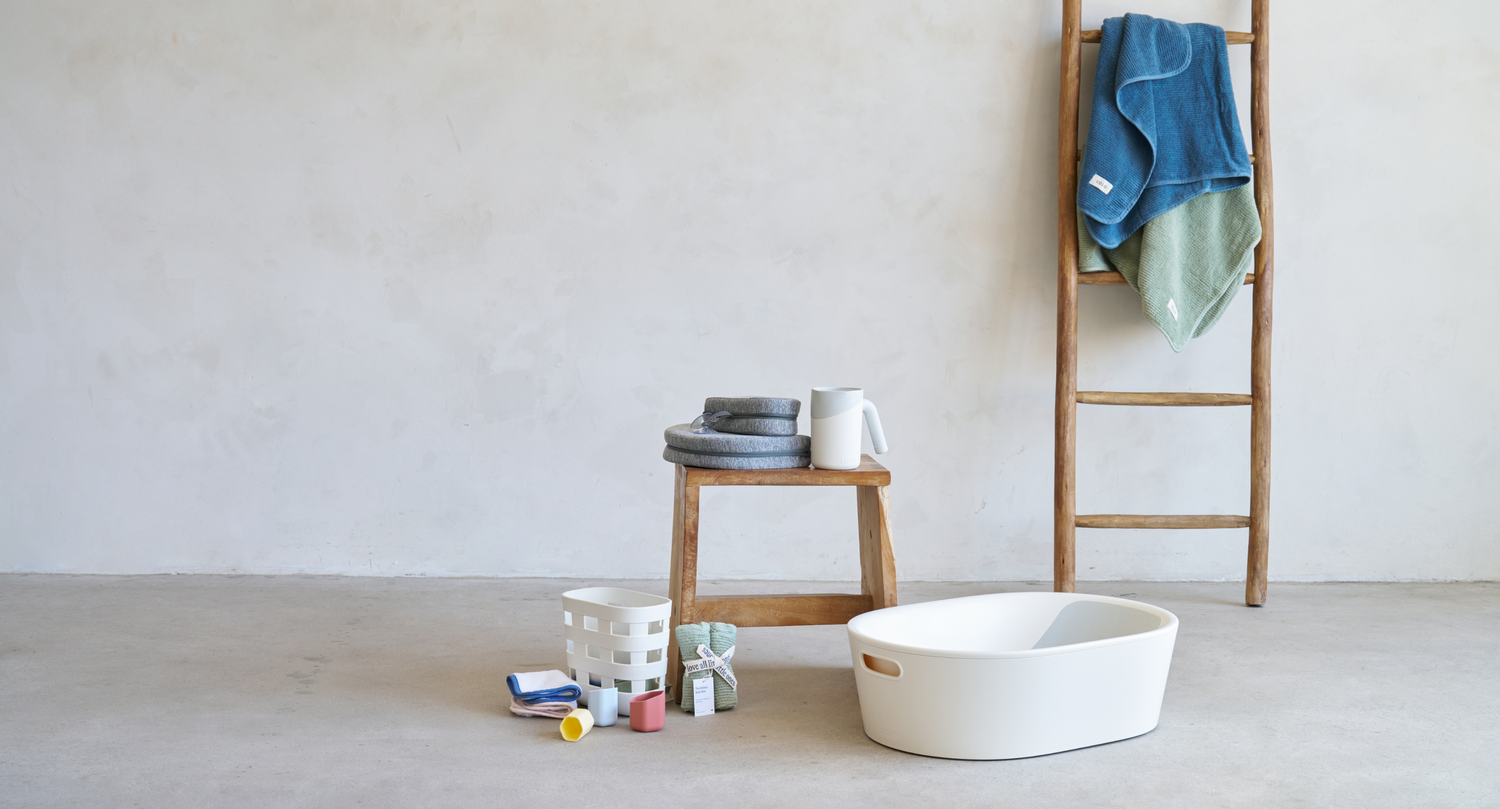 The Bathtub, Knee and Elbow Savers, Rinse Cup, Bath toy bin, stacking cups and ribbed hooded towels with a bow and holiday decorations in an empty room