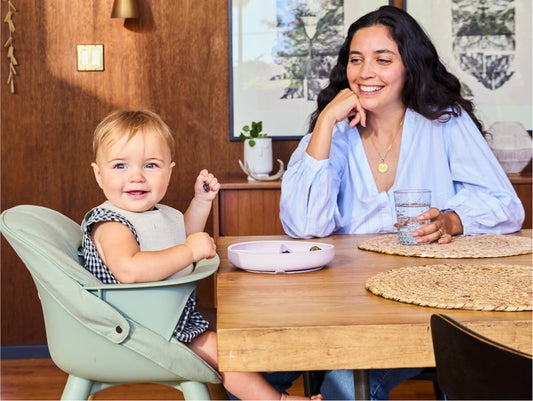 Baby eating food at table with mom