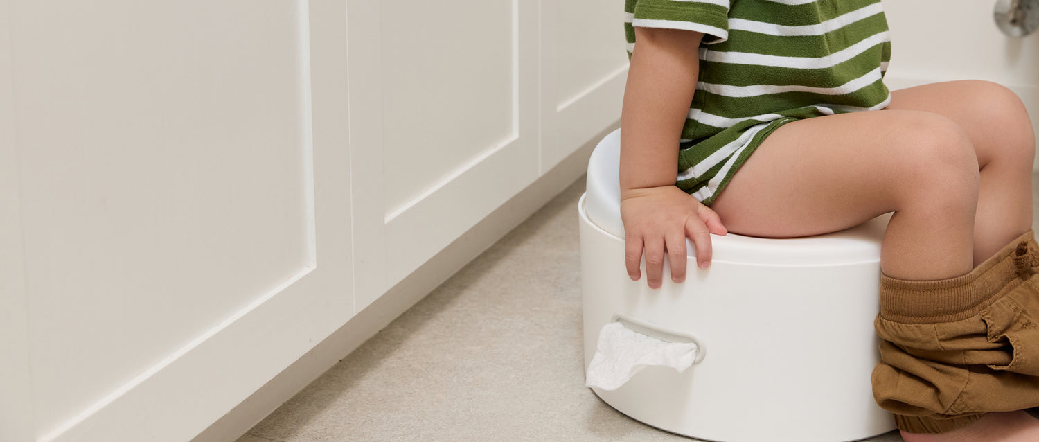 Child sitting on a white potty chair in a bathroom.