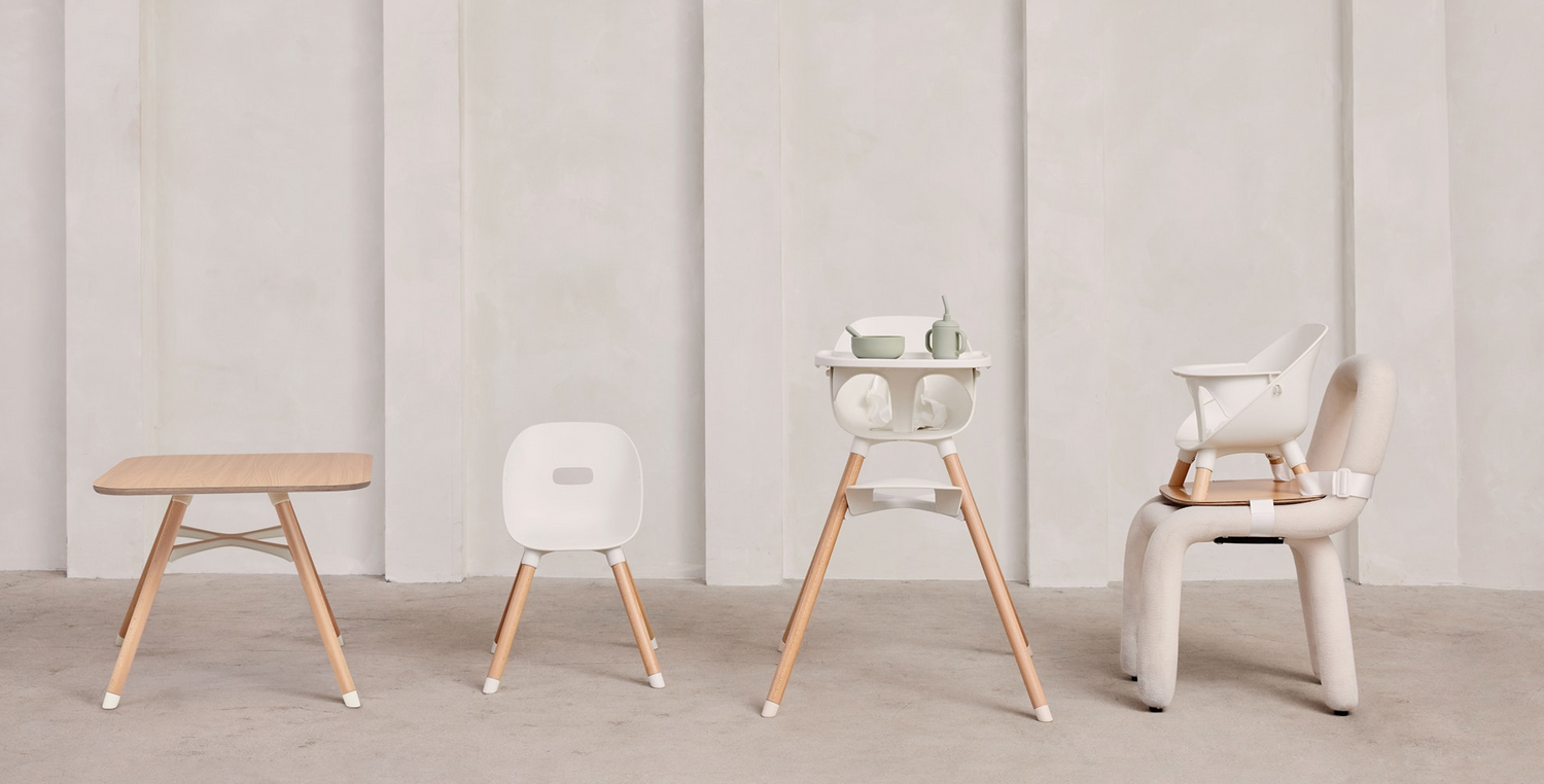 Set of modern baby furniture including a high chair, table, and chairs on a neutral background