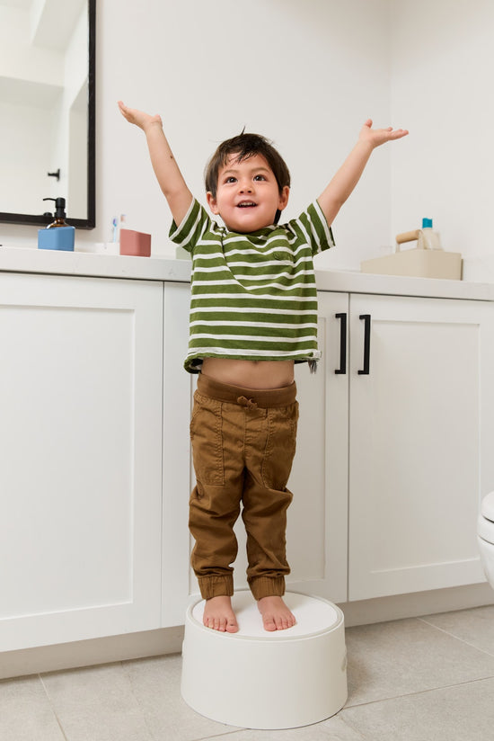 Child standing on a stool in a bathroom with arms raised